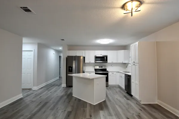 a kitchen with stainless steel appliances a refrigerator a stove top oven a sink dishwasher and white cabinets with wooden floor