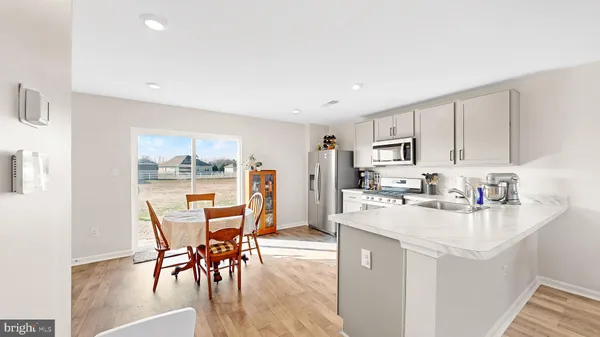a kitchen with stainless steel appliances kitchen island granite countertop a stove a refrigerator a sink a dining table and chairs with wooden floor