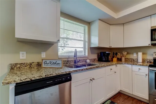 a kitchen with granite countertop stainless steel appliances white cabinets sink and window