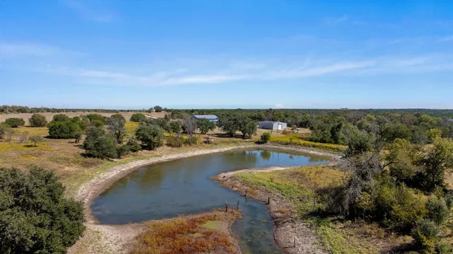 a view of a lake with lawn chairs and large trees