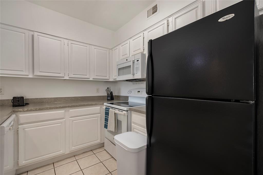 14277 Preston Road, Unit 823 Dallas, TX 75254 - Photo 13 of 31 Kitchen featuring white cabinetry, light-toned countertops, tile flooring, and white and black appliances including a built-in microwave, range, and refrigerator