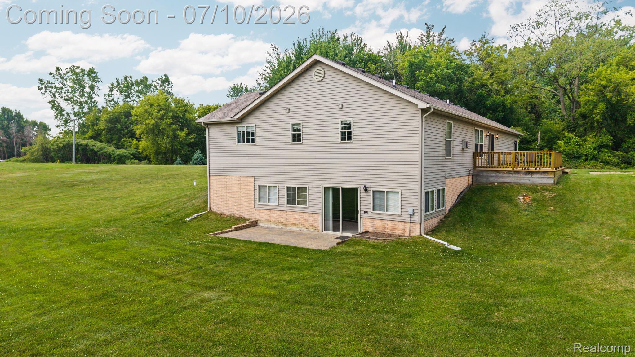 3144 North Nicholson Road Fowlerville, MI 48836 - Photo 15 of 70 Expansive rear exterior featuring light-colored siding, a multi-level design, a ground-level patio, a raised wooden deck, and a surrounding green landscape