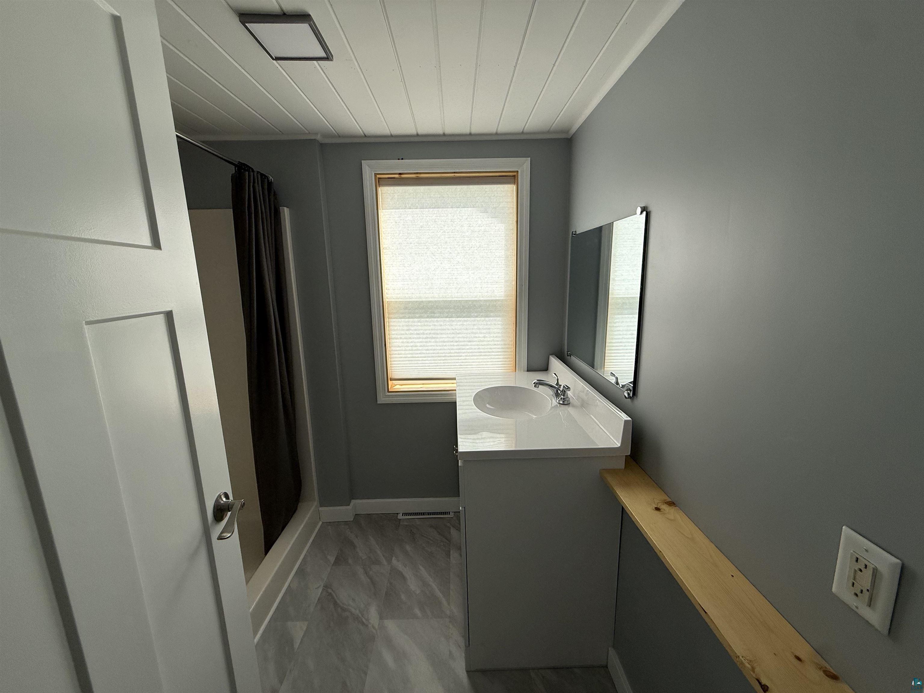 3841 Haines Road Hermantown, MN 55811 - Photo 8 of 11 Bathroom featuring a white vanity with integrated sink, a rectangular mirror, and gray wood-finish flooring