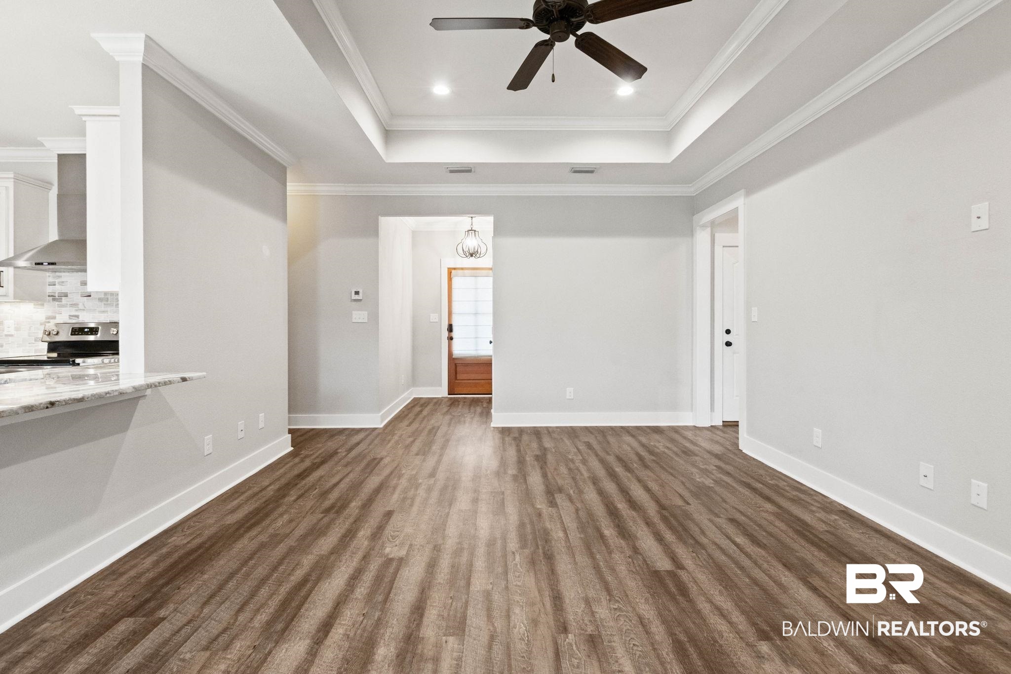 17376 Bankhead Boulevard Fairhope, AL 36532 - Photo 16 of 73 Unfurnished living room featuring a raised ceiling, dark wood-style floors, a ceiling fan, crown molding, and a chandelier
