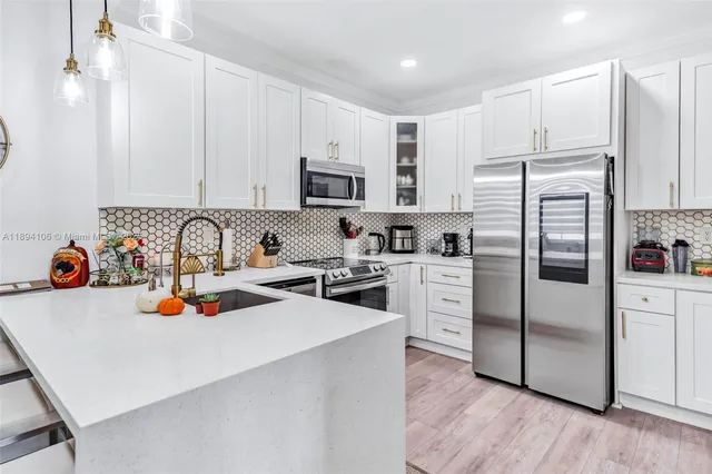 a kitchen with stainless steel appliances a refrigerator a sink a stove and white cabinets