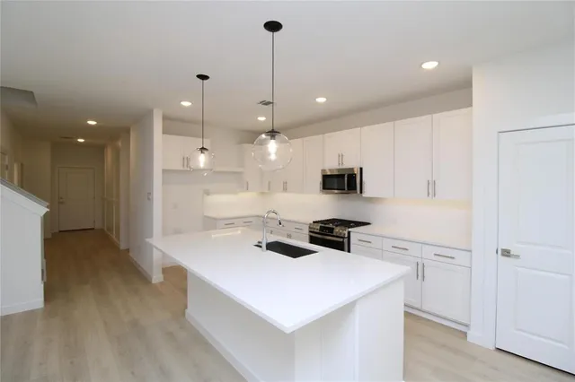 a kitchen with stainless steel appliances a stove a sink a refrigerator and white cabinets with wooden floor