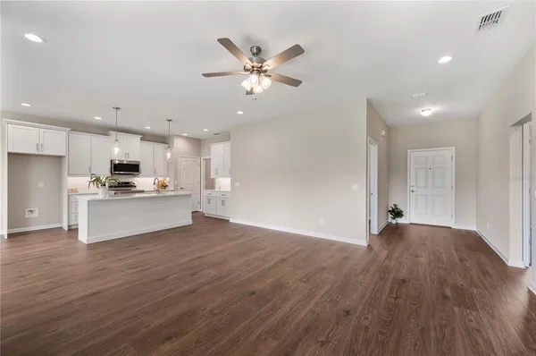 a view of an empty room with wooden floor and a kitchen