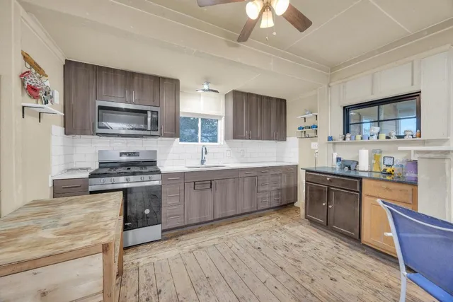 a kitchen with stainless steel appliances kitchen island granite countertop a stove top oven a sink dishwasher a dining table and chairs with wooden floor