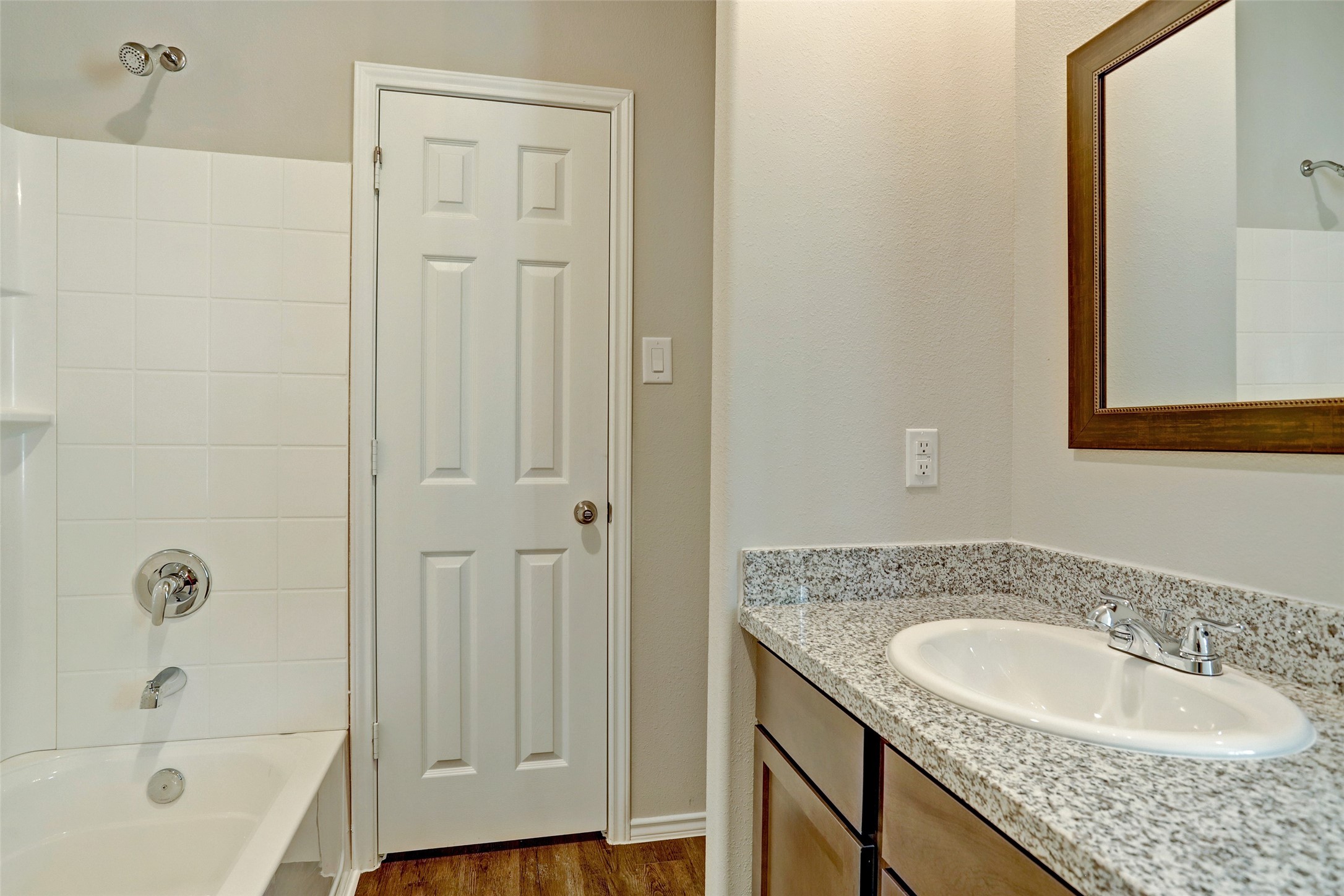 409 South 12th Street, Unit B Conroe, TX 77301 - Photo 13 of 14 This bathroom features a clean design with a white bathtub and shower, granite countertop with a single sink, and a large mirror. The neutral walls and wood-style flooring add warmth and elegance.