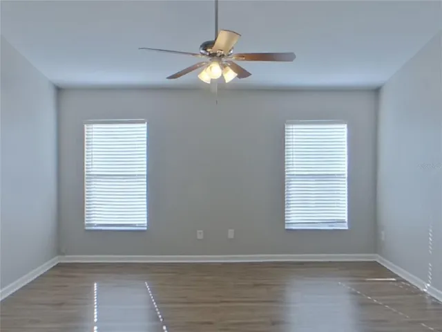 a view of an empty room with wooden floor and a ceiling fan