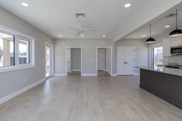 a view of an empty room with kitchen and window