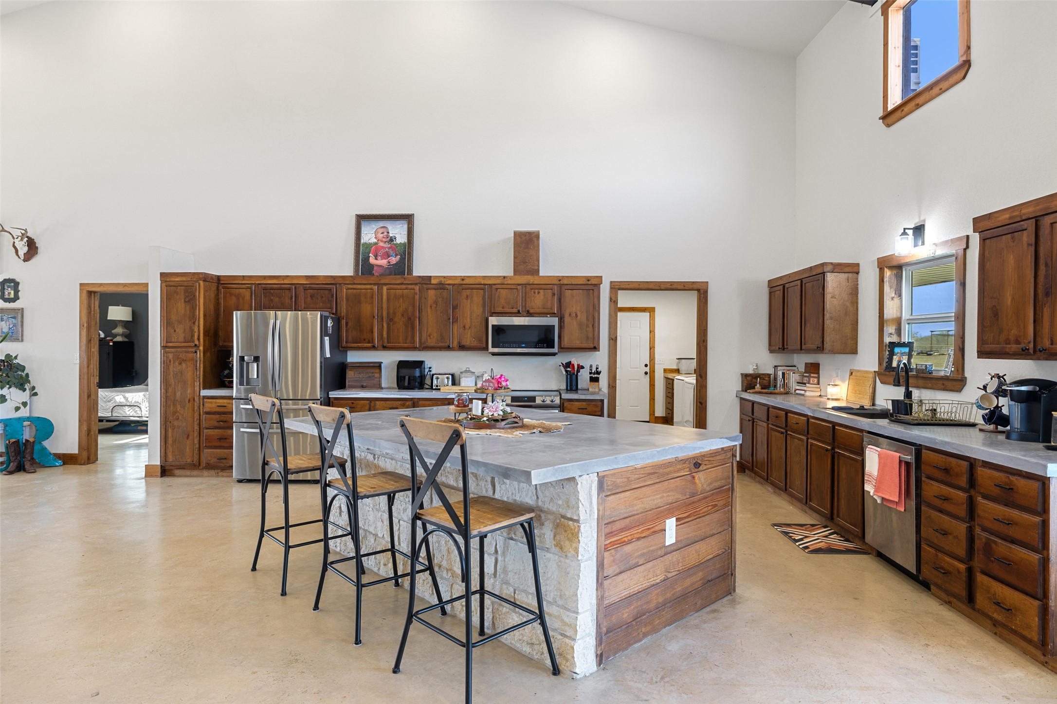 664 Martindale Falls Road Martindale, TX 78655 - Photo 10 of 21 Spacious kitchen featuring a large stone and wood-paneled island, stainless steel appliances, extensive dark wood cabinetry, light-toned countertops, and soaring ceilings