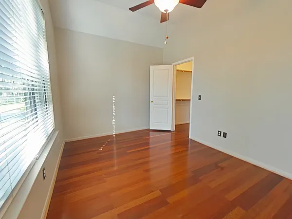an empty room with wooden floor chandelier fan and windows
