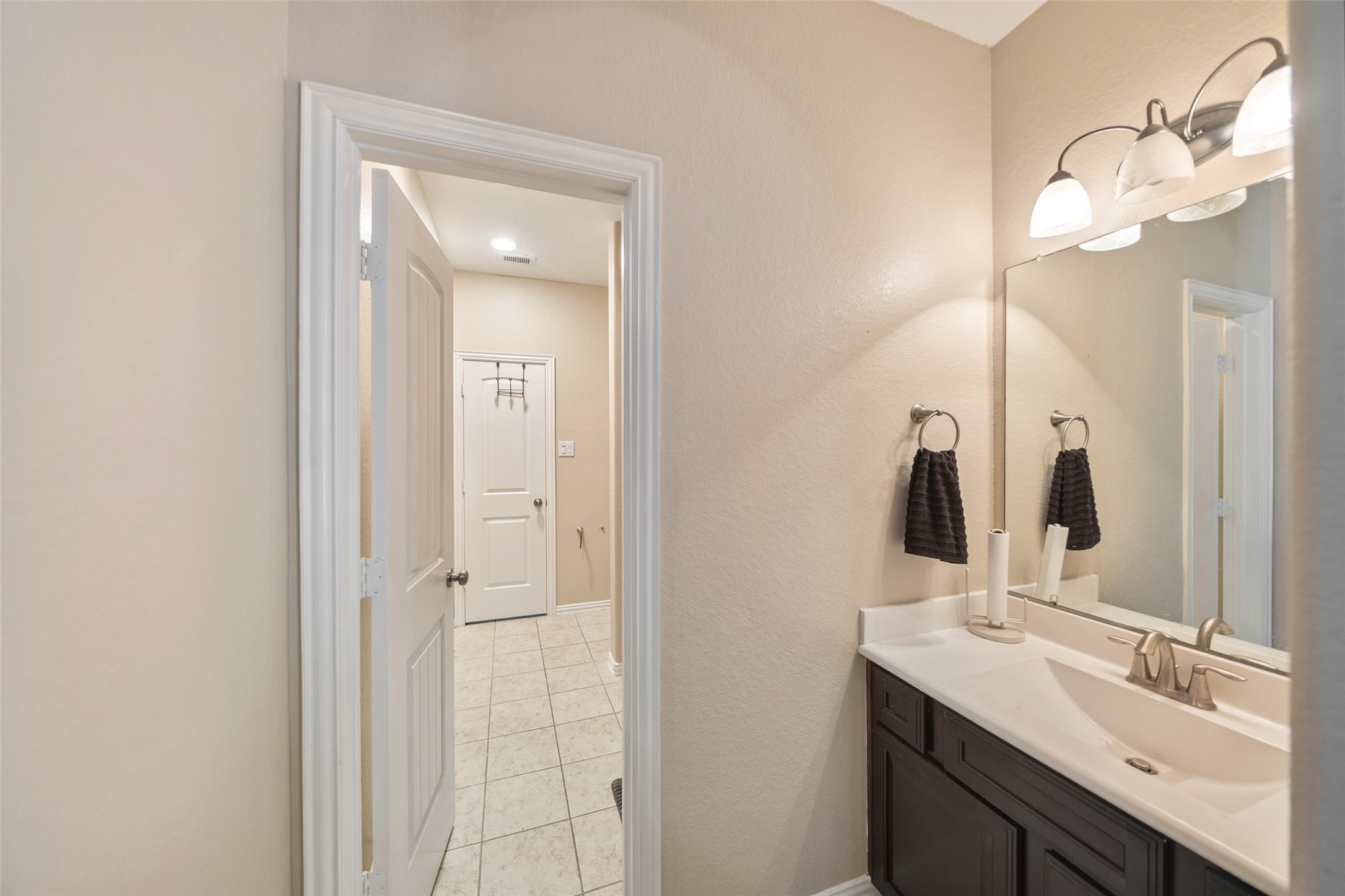 4747 Abercorn Street Rosharon, TX 77583 - Photo 27 of 46 This photo showcases a well-lit jack-and-jill bathroom with a modern vanity, large mirror, and overhead lighting. The room features neutral walls and tile flooring, with a view into a hallway.