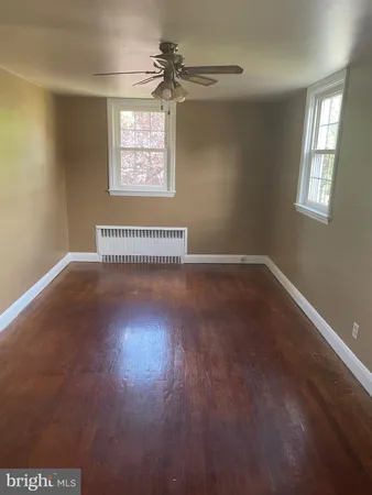 an empty room with wooden floor windows and fan
