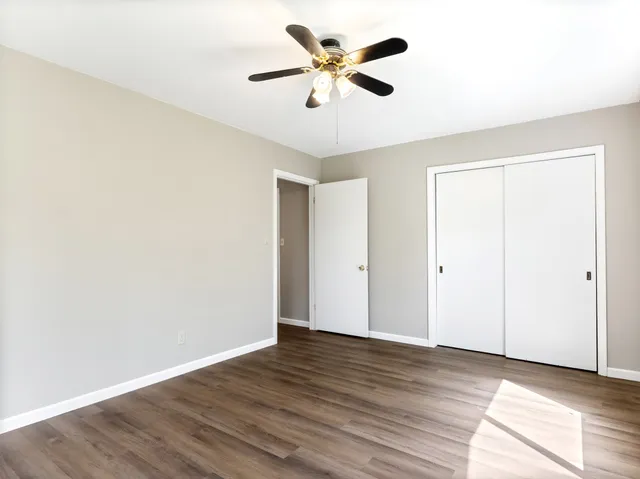 a view of an empty room with window a ceiling fan and wooden floor