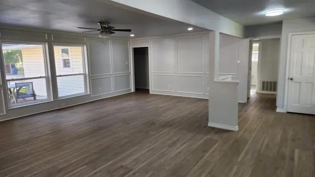 a view of an empty room with wooden floor and a kitchen