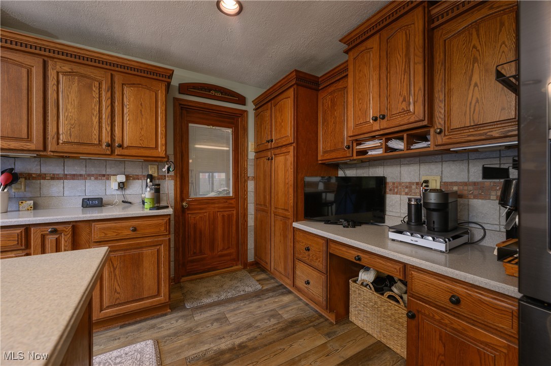 2856 Shellhart Road Barberton, OH 44203 - Photo 15 of 27 Kitchen featuring a textured ceiling, brown cabinetry, built in study area, light countertops, and backsplash