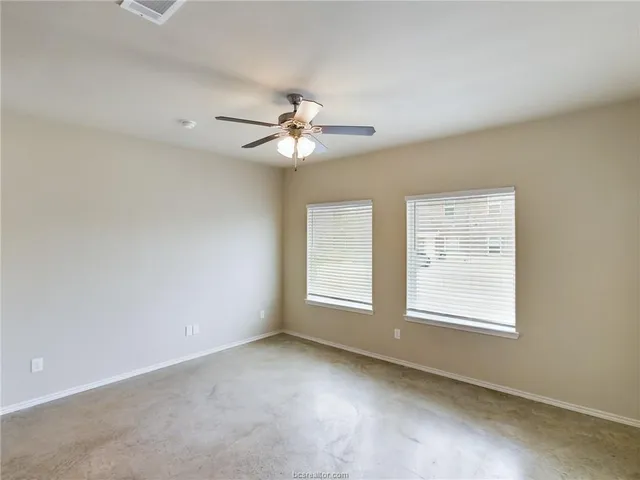 an empty room with chandelier fan and windows