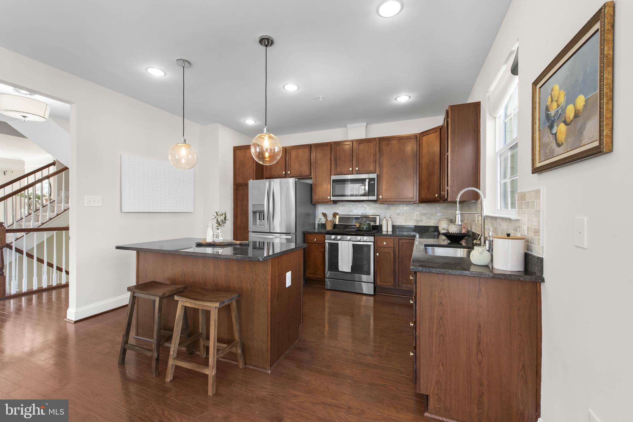 5948 Logans Way Ellicott City, MD 21043 - Photo 16 of 44 a kitchen with kitchen island granite countertop a stove a sink a oven a dining table and chairs with wooden floor