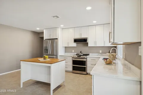 a kitchen with stainless steel appliances granite countertop a sink stove refrigerator and white cabinets with wooden floor