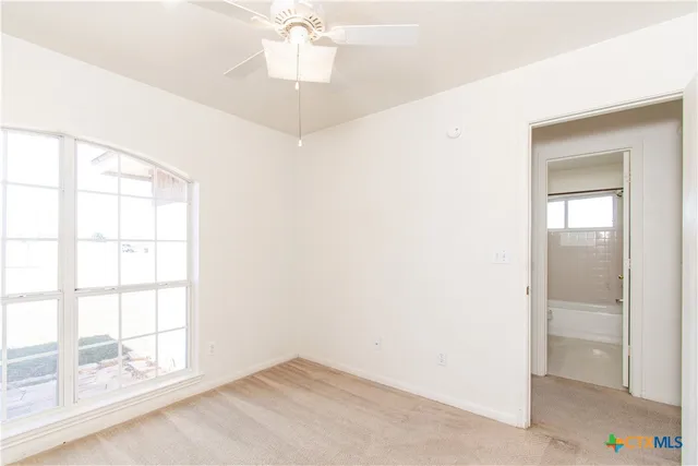 an empty room with chandelier fan and windows