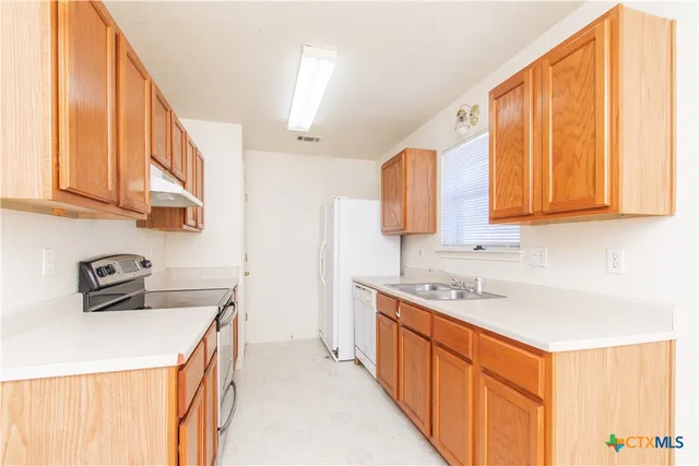 a kitchen with stainless steel appliances a sink a stove a refrigerator cabinets and a window