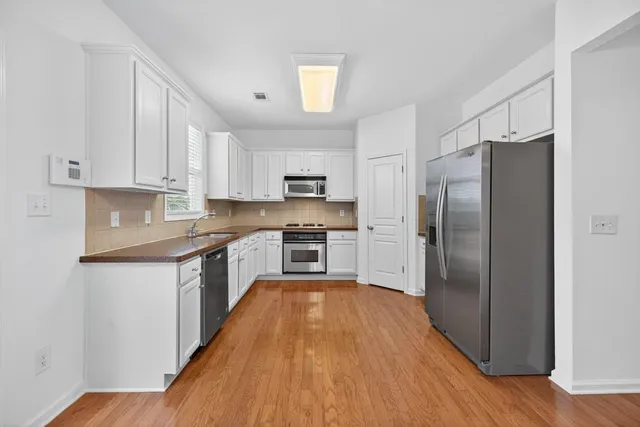 a large kitchen with a refrigerator a sink dishwasher a stove and white cabinets with wooden floor