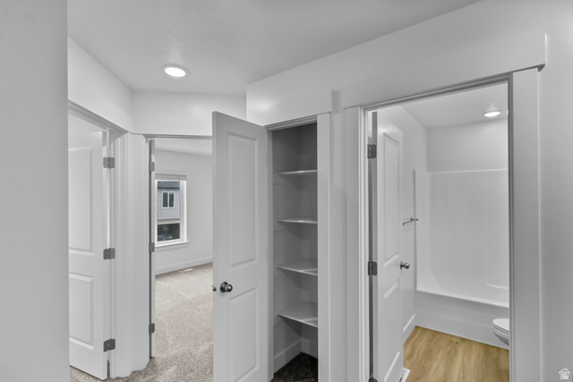 3014 South 265th Street West Logan, UT 84321 - Photo 14 of 25 Hallway featuring a built-in linen closet with shelving, leading to a bedroom with carpeted flooring and a window, and a bathroom with wood-finish flooring and a white tub/shower combination