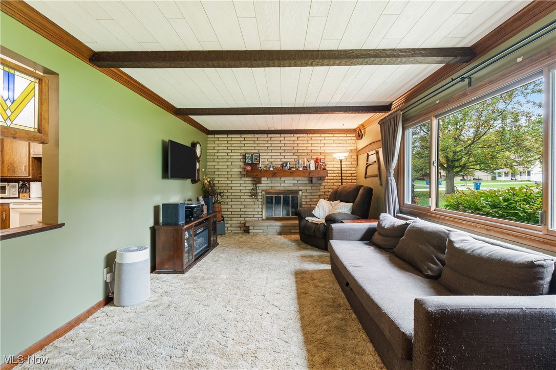 Carpeted living room featuring wood ceiling, a brick fireplace, beam ceiling, and ornamental molding