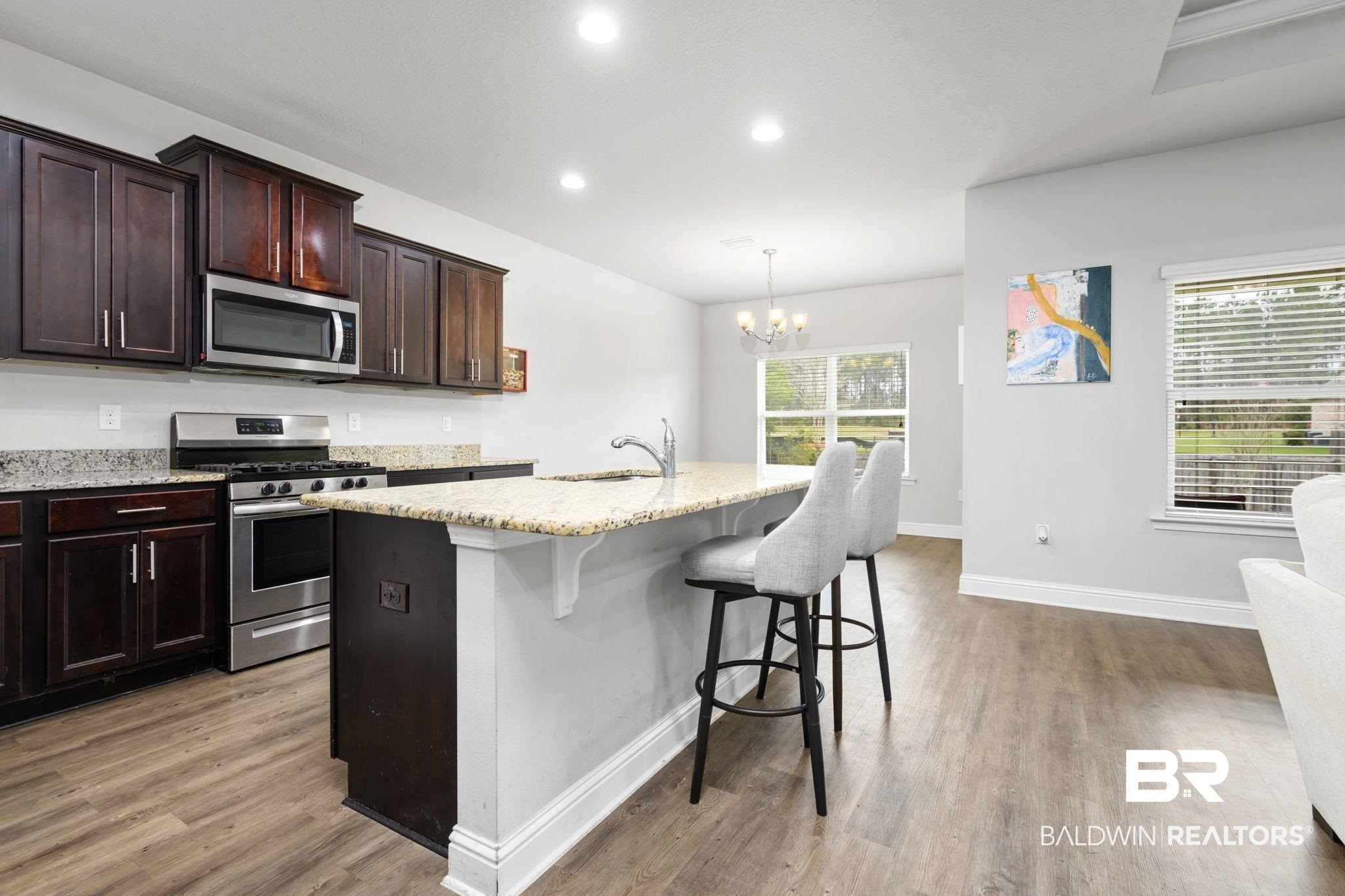 12693 Waxwing Avenue Daphne, AL 36527 - Photo 18 of 43 Kitchen with stainless steel appliances, a breakfast bar area, light wood-style flooring, light stone countertops, and a kitchen island with sink