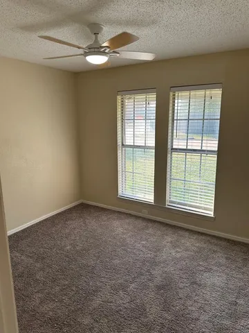 an empty room with chandelier fan and windows