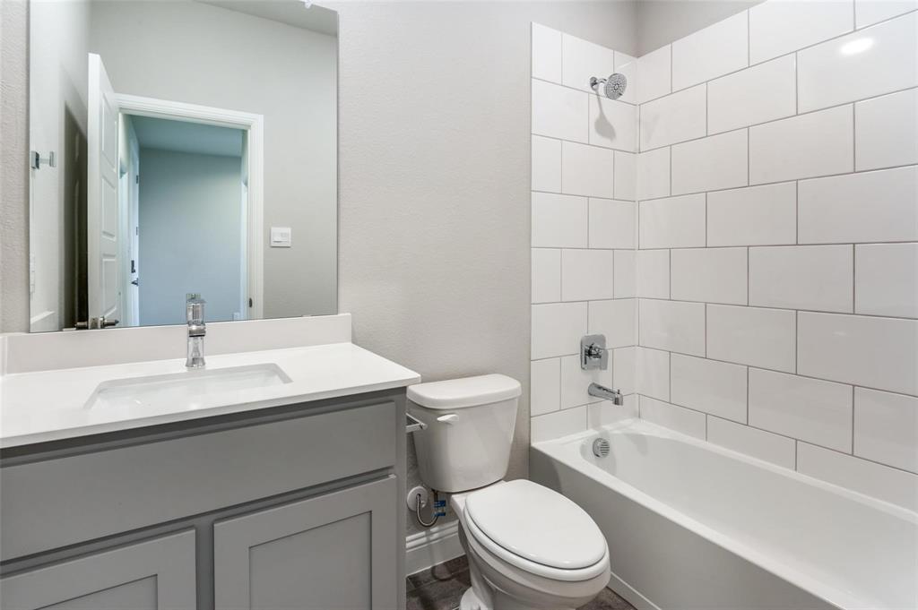 1517 Razorbill Road Denton, TX 76205 - Photo 18 of 25 Bathroom featuring a white subway tile shower surround, a built-in bathtub, a toilet, a vanity with a white countertop and an undermount sink, and wood-finish flooring