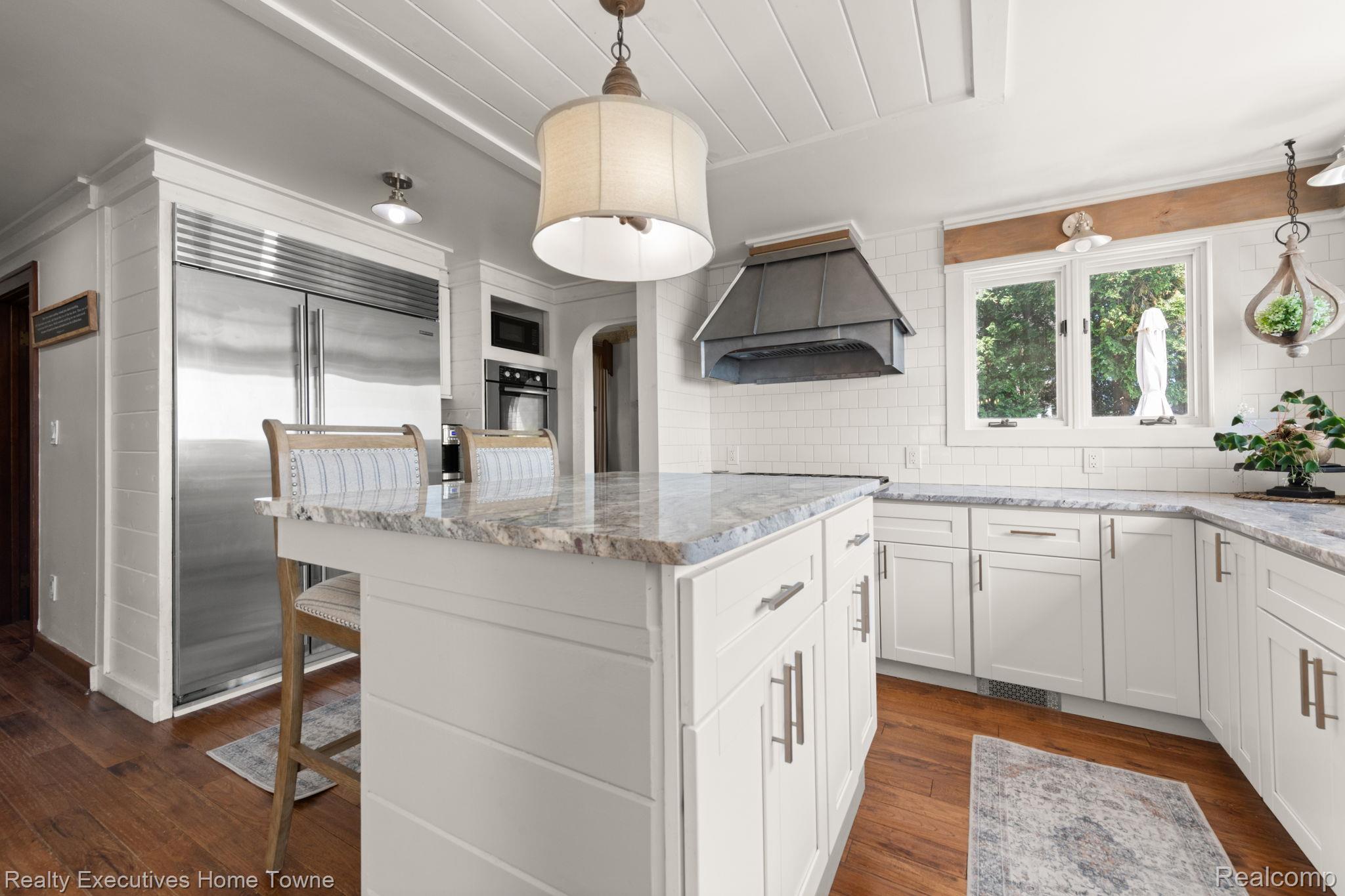 8308 Lakeshore Road Fort Gratiot, MI 48059 - Photo 40 of 79 Kitchen featuring a central island with a stone-finish countertop, white cabinetry, integrated stainless steel refrigerator, white subway tile backsplash, and wood-finish flooring