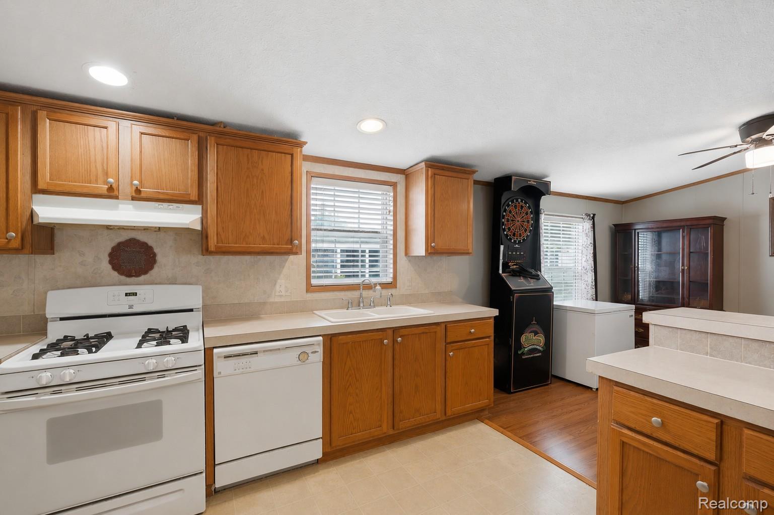 Spacious kitchen featuring warm wood cabinetry, white gas range, tile countertops, stainless steel dishwasher, and abundant counter space
