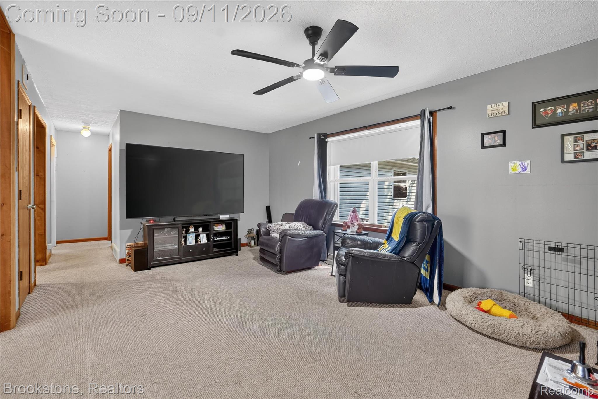 1812 South Steel Road Merrill, MI 48637 - Photo 8 of 39 Carpeted living area with a ceiling fan, a large window, and a hallway with wood-paneled doors