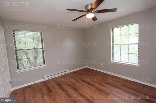 an empty room with wooden floor ceiling fan and windows