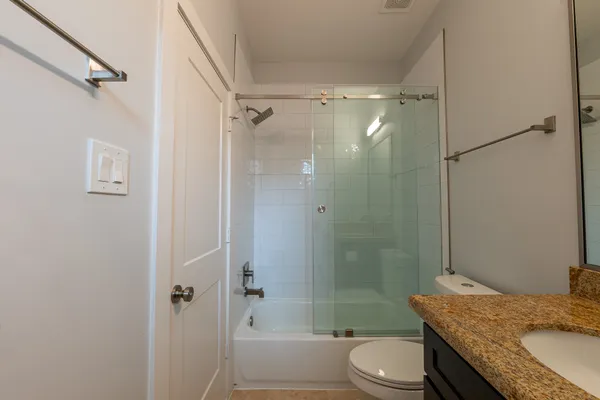 a bathroom with a granite countertop tub sink vanity mirror and toilet