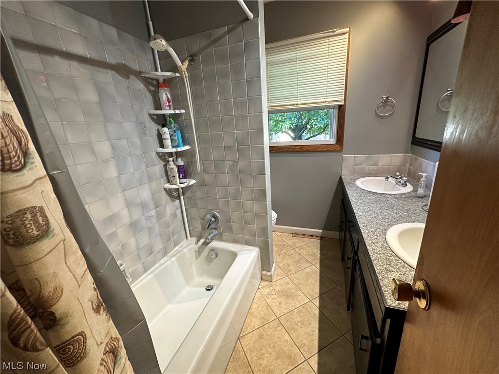 Full bathroom featuring double sink vanity, tiled shower / bath combo, mirror, and light tile floors