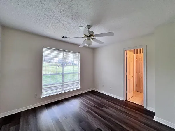 an empty room with wooden floor fan and windows