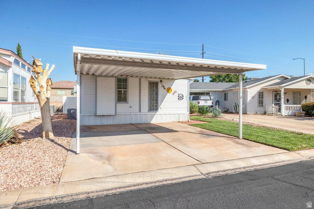 2990 East Riverside Drive, Unit 173 St. George, UT 84790 - Photo 37 of 38 Exterior featuring white horizontal siding, a covered carport, concrete driveway, decorative glass block window, and xeriscape landscaping