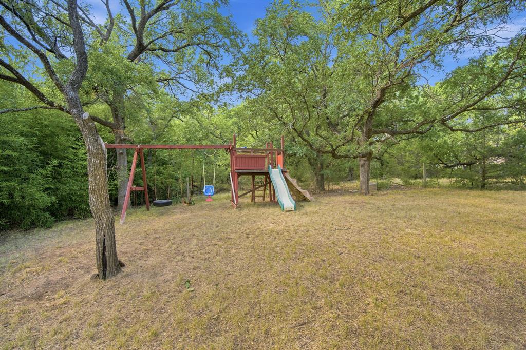 3325 Dove Creek Road Cleburne, TX 76031 - Photo 24 of 40 Expansive outdoor space featuring a wooden play structure with a slide, a swing set, and mature trees providing natural shade