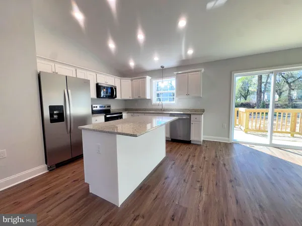 a kitchen with stainless steel appliances granite countertop a refrigerator a sink dishwasher a stove top oven and wooden floor