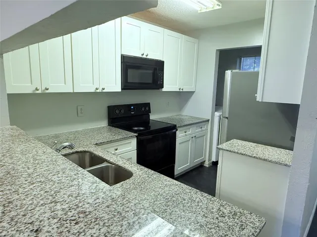 a kitchen with stainless steel appliances kitchen island granite countertop white cabinets a refrigerator and a stove