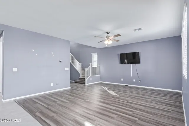 a view of an empty room with wooden floor and a ceiling fan