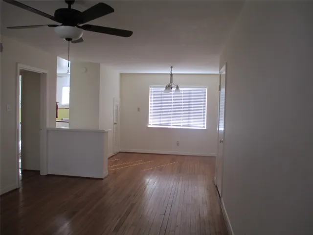 an empty room with wooden floor chandelier fan and windows