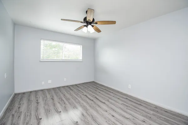 an empty room with wooden floor chandelier fan and windows