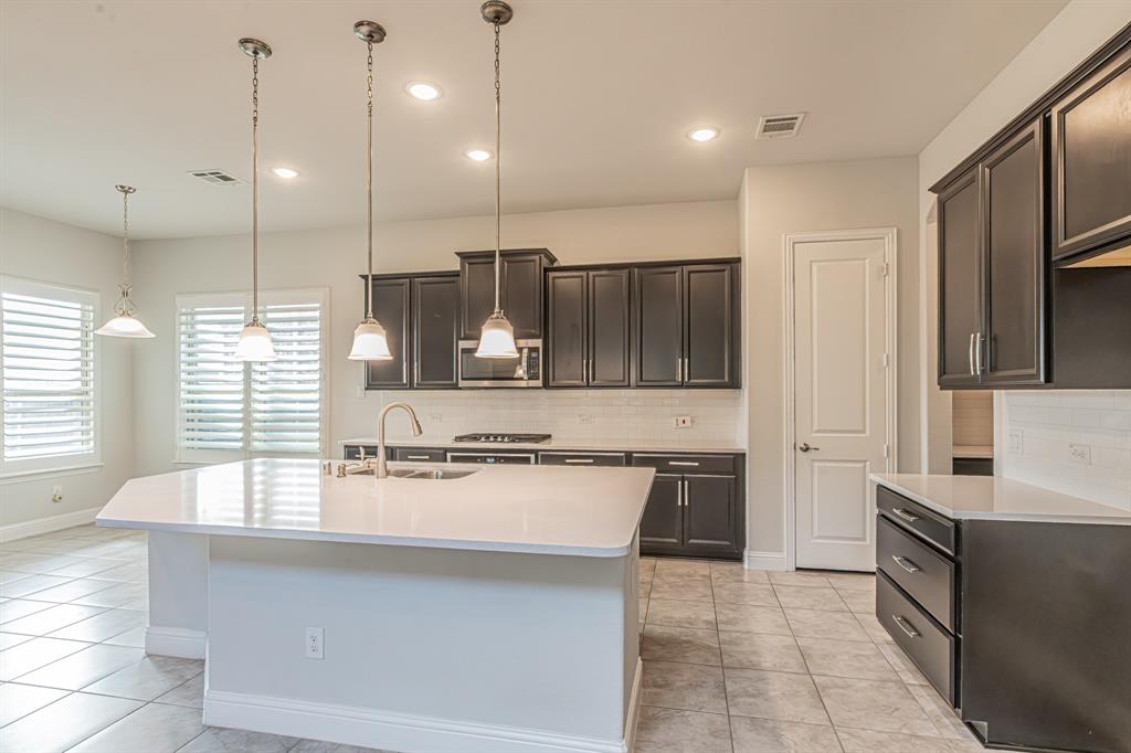 304 Adam Way Euless, TX 76040 - Photo 13 of 39 Kitchen featuring tasteful backsplash, a center island with sink, light stone counters, stainless steel appliances, and dark wood finish cabinets