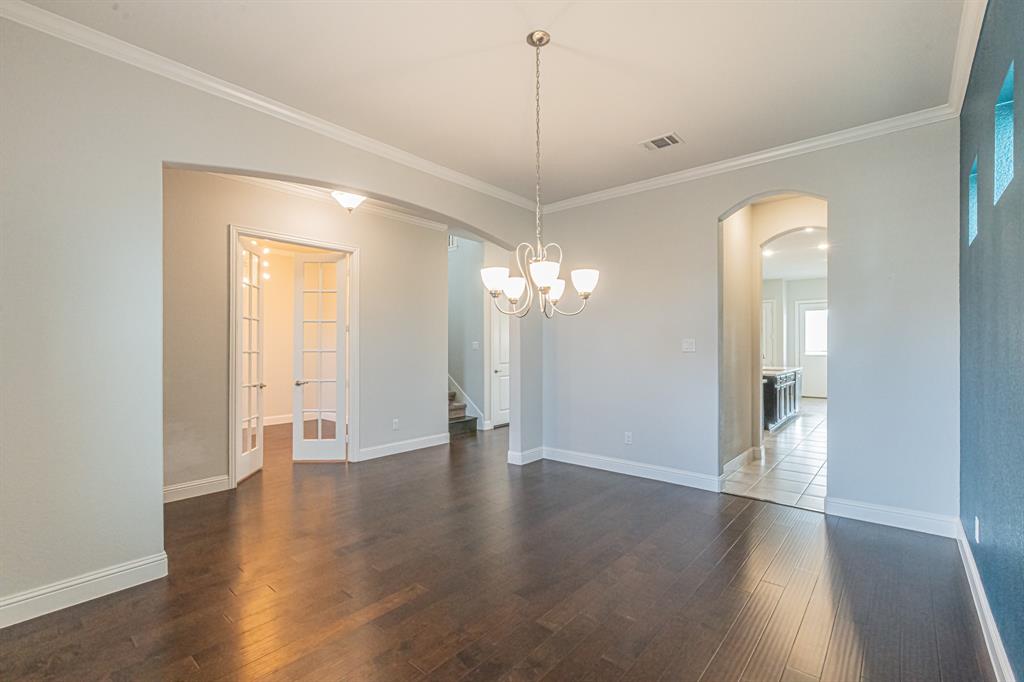 304 Adam Way Euless, TX 76040 - Photo 8 of 39 Empty room featuring dark wood-style flooring, suspended lighting, ornamental molding, and arched walkways