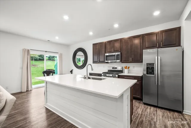 a kitchen with kitchen island granite countertop a stove a sink dishwasher a refrigerator cabinets and wooden floor